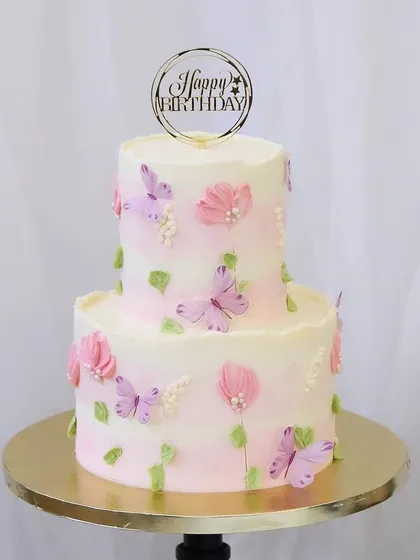 A delicate two-tiered cake with a soft pink watercolor effect. This design is adorned with beautiful wafer paper butterflies and hand-piped flowers, creating a whimsical and light feel.