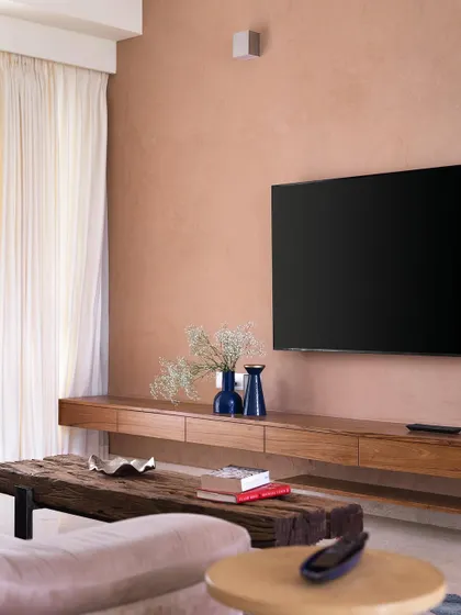The family space in 'A Walk in the Clouds' is a cozy area for relaxation, featuring a comfortable sofa, a rustic wooden bench, and a TV against a warm, textured peach wall.
