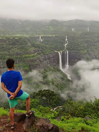 A trekker looking out at the magnificent Kathaldar waterfalls in Maharashtra, with clouds floating below.