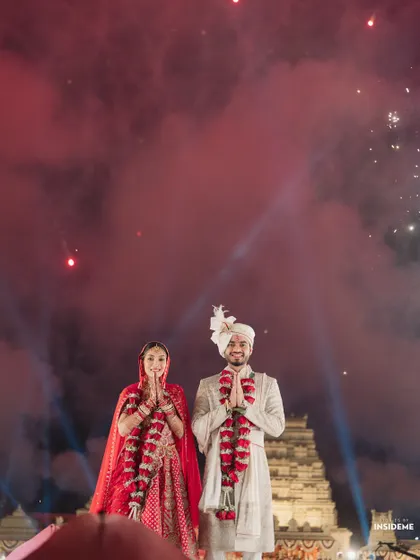 A moment of gratitude and joy. The couple greets their guests after the varmala, surrounded by red smoke and a sky lit with fireworks, creating a powerful and colorful memory.