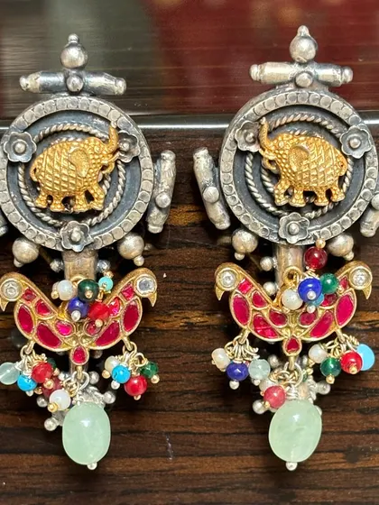 These fusion earrings feature a powerful elephant motif in gold plate set against an oxidised silver background. The colourful enamel work and dangling beads add a playful yet regal touch.