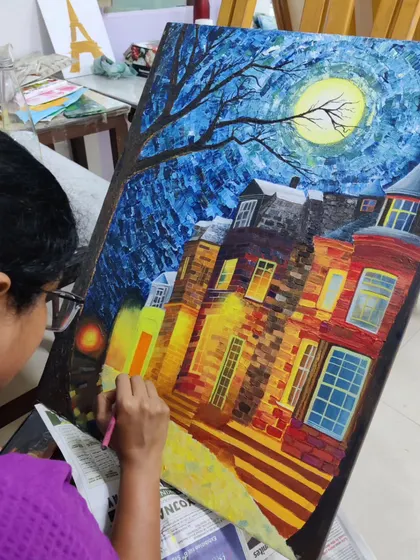 A close-up of a student adding fine details and highlights to the windows and streetlights of her acrylic cityscape, bringing the scene to life.