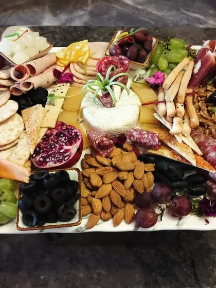 This is our grand charcuterie platter, a feast of textures and flavors. It features a curated selection of imported cheeses, cured meats, fresh fruits like pomegranates and grapes, assorted nuts, olives, and artisanal crackers.