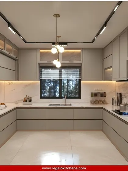 A spacious and bright U-shaped kitchen in a uniform light grey. The design is clean and minimalist, with ample storage and counter space. The large window allows for plenty of natural light.
