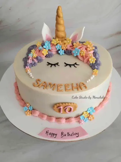 A cute unicorn themed cake for a 10th birthday. This no-fondant design features a unicorn face with sleepy eyes and a crown of colourful, hand-piped flowers.