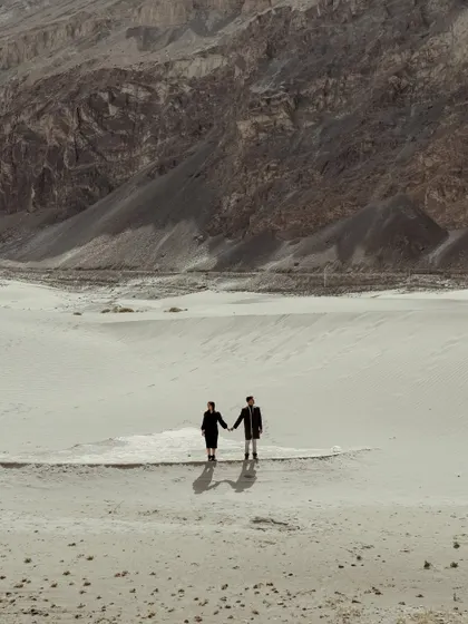 Walking hand-in-hand through the sand dunes of Ladakh, with the mountains as your witness. This wide shot emphasizes the scale of your adventure and the journey you're on together.