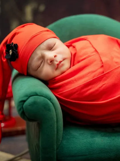 A close-up of a newborn wrapped in a vibrant red swaddle, sleeping soundly on a miniature green sofa.