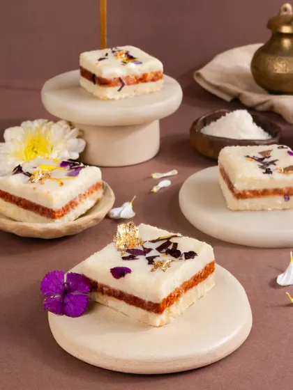 Square pastries with a beautiful white layer and edible flower garnish, styled on minimalist marble coasters.