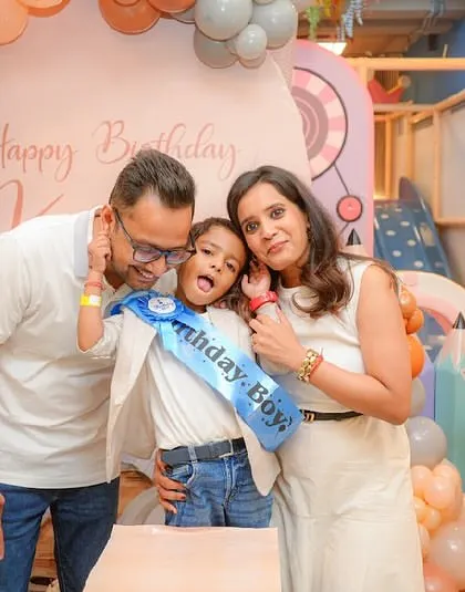 The birthday boy makes a funny face while his parents smile, capturing a fun, candid moment at the cake table.
