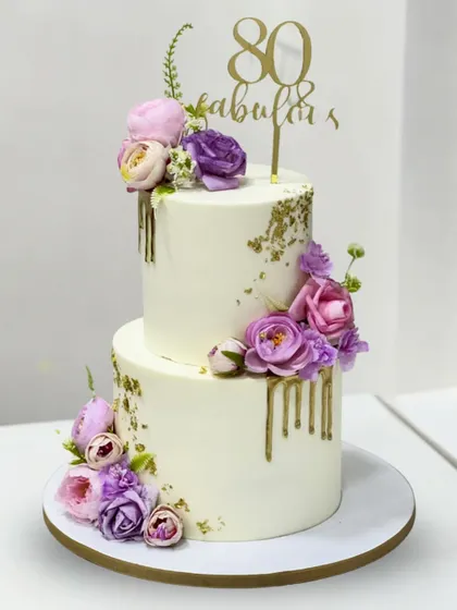 80 and absolutely fabulous! This two-tier floral cake celebrates a graceful milestone in an elegant way, adorned with soft pastel flowers and delicate golden drips.