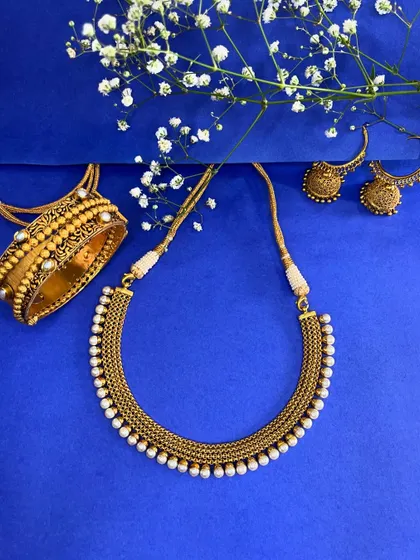 Shine like never before with this golden ensemble. A pearl-lined neckpiece, matching jhumka earrings, and a statement kadda bangle that blend tradition and elegance perfectly.