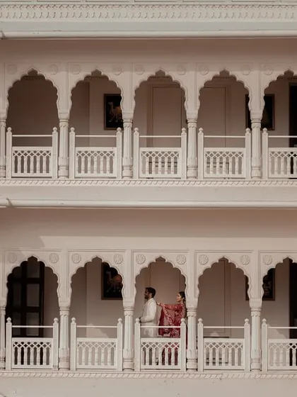 The palace architecture frames the couple on a balcony, creating a sense of timeless romance and quiet intimacy amidst the grandeur. This shot showcases our eye for creative composition in royal wedding photography.