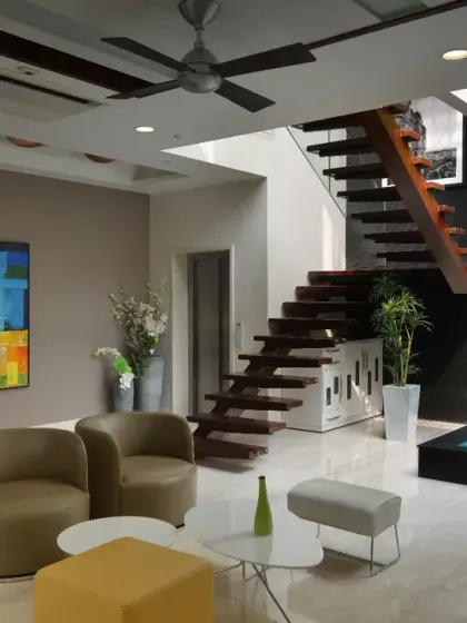 The first-floor lounge at Gupta Residence is centered around a tranquil water feature with a Buddha statue and vertical garden. A floating wooden staircase adds architectural drama, while vibrant artwork brings sophistication and warmth.
