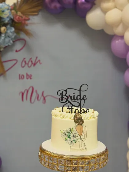 A close-up of the beautiful cake for a "Soon to be Mrs" party. Our backdrop in soft lavender with a white and purple balloon arch provides the perfect setting for the dessert table.