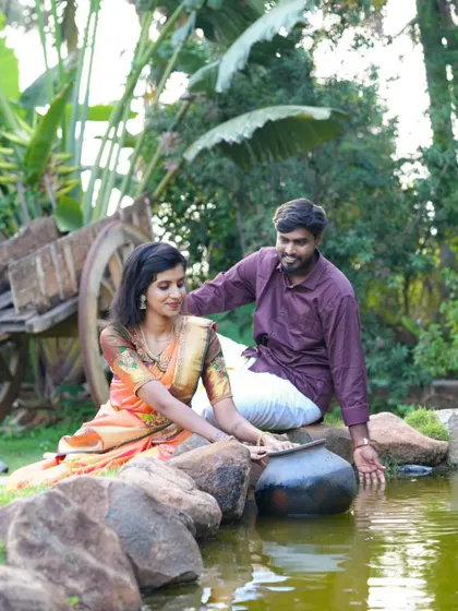 A romantic, rustic-themed pre-wedding photo by a small pond. The traditional outfits and setting create a charming, earthy vibe.