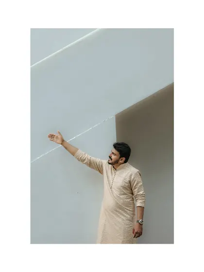 A stylish portrait of the groom against a minimalist white wall, showcasing his modern ethnic attire.
