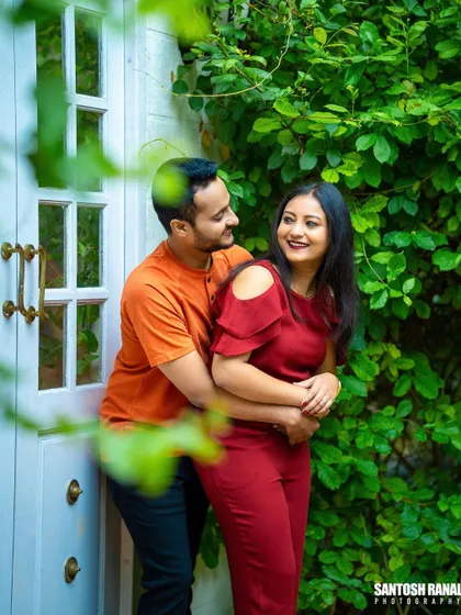 A sweet and casual portrait of a couple embracing by a white door and green vines.