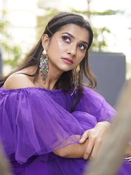 A thoughtful pose showing off the artistic makeup. The long, dramatic earrings and the purple tulle of the dress add to the high-fashion feel.