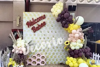 This "Welcome Babee" backdrop features a honeycomb pattern and is framed by a unique balloon garland. The use of pampas grass and sunflowers adds a rustic, boho touch to the bee-themed baby shower.