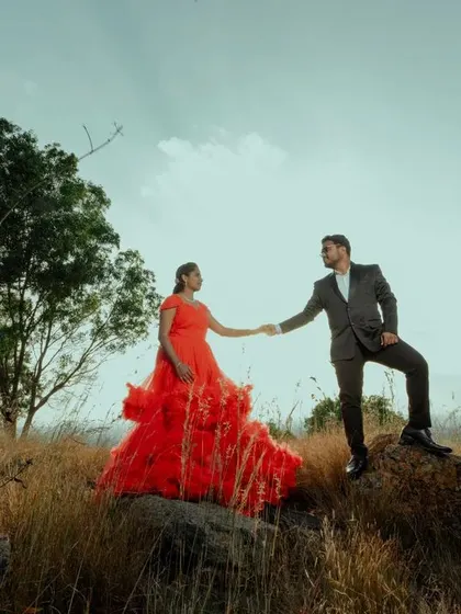 A powerful and dramatic pose on a rocky outcrop against the sky. The bride's red dress and the couple's strong stance create an epic, storybook image.