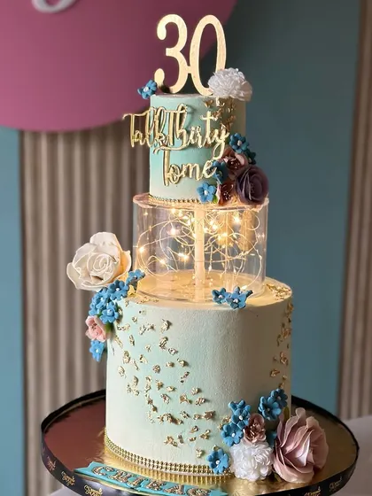 Dreamy layers in white and sky blue. This tall cake for a 30th birthday features a glowing light-up tier, delicate sugar flowers, and a beautiful textured finish.
