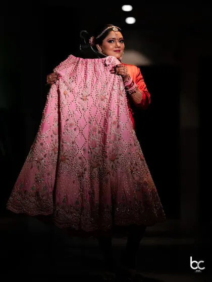 A creative shot of the bride holding up her intricately embroidered pink lehenga skirt before getting dressed for her big day.