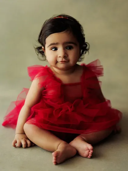 A simple and beautiful portrait of a baby girl in a red tutu, sitting gracefully. The soft green backdrop complements her outfit perfectly.