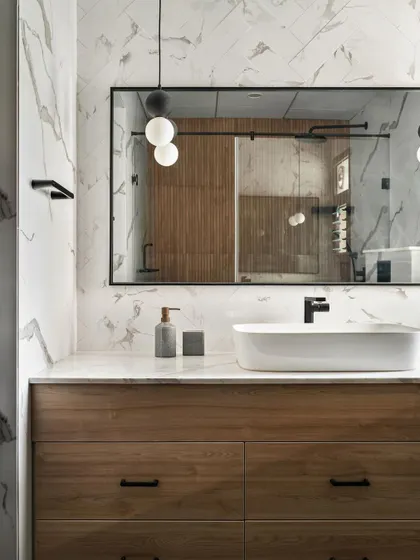 A modern bathroom with a wood vanity and a large mirror. The walls are clad in large-format marble-look tiles for a seamless and sophisticated finish.