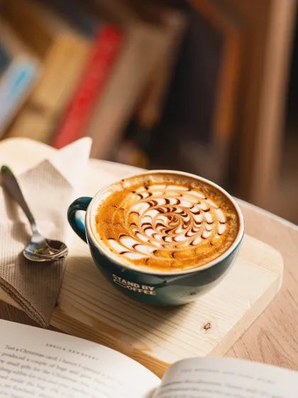 A beautifully crafted mocha with intricate latte art, set in a cozy reading scene. This lifestyle approach helps sell the experience, not just the coffee.