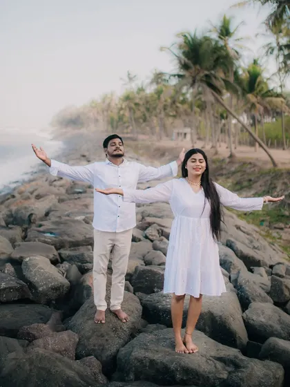 A playful and serene moment as a couple stands on the rocks by the sea with their arms outstretched.