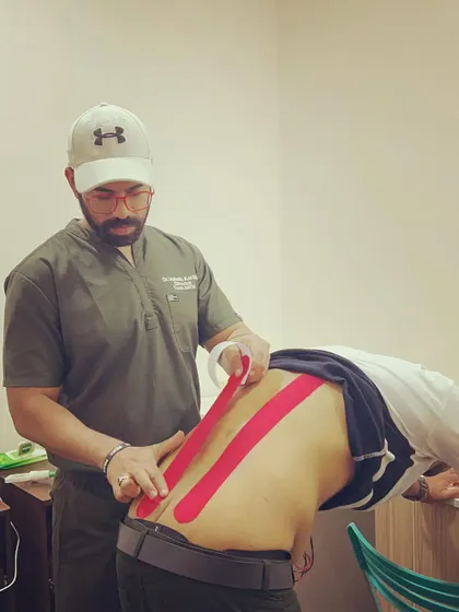 A therapist applies red kinesio tape along a client's spine. This method helps to decompress the area and provide sensory feedback to encourage better posture and movement.