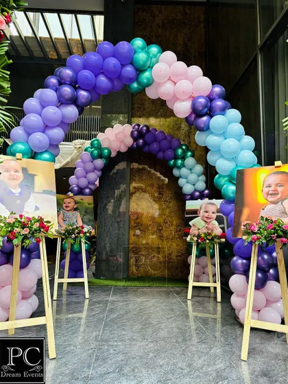 A welcoming entrance for a mermaid-themed birthday party. Balloon arches in shades of purple, pink, and teal create a magical tunnel, flanked by personalized photo easels of the birthday girl.