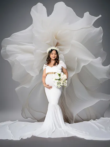 A stunning solo portrait of the mom-to-be in a white gown with a dramatic fabric fan effect behind her. This artistic shot is both elegant and powerful.