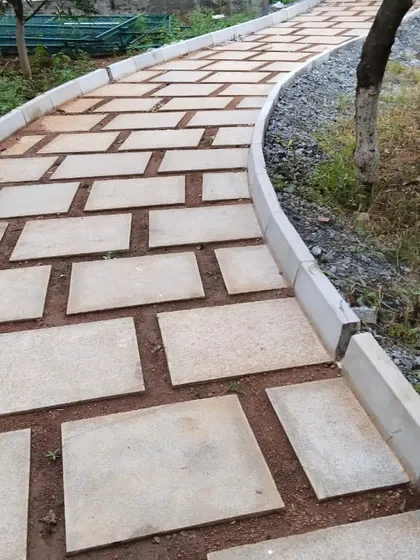 A curving walkway made of rectangular stone pavers set in red soil, with a concrete curb defining the edge. This shows the construction of a durable and well-defined garden path.