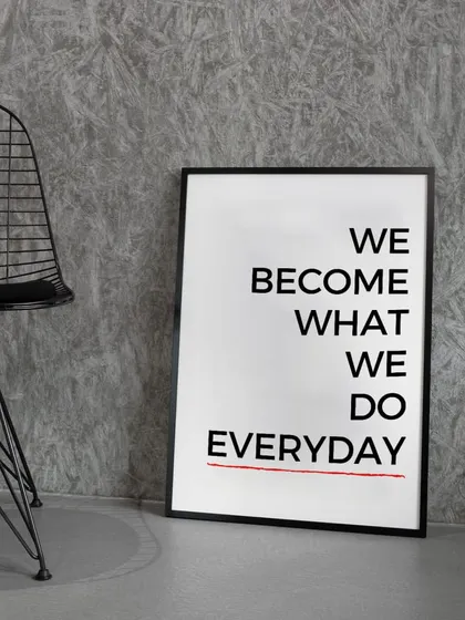The "We Become What We Do Everyday" print, displayed in a sleek black frame against a textured grey wall. This minimalist presentation is perfect for a modern, industrial-inspired space.