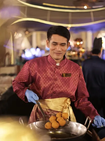 A chef from our Thai culinary team carefully fries traditional delicacies. His smile and technique demonstrate the authentic expertise we bring to our international cuisine offerings.