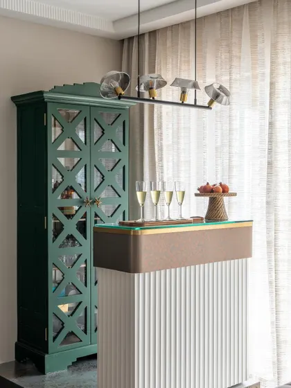 A chic and modern home bar setup. The fluted white bar counter, elegant green cabinet, and modern pendant lighting create a sophisticated spot for enjoying champagne with guests.