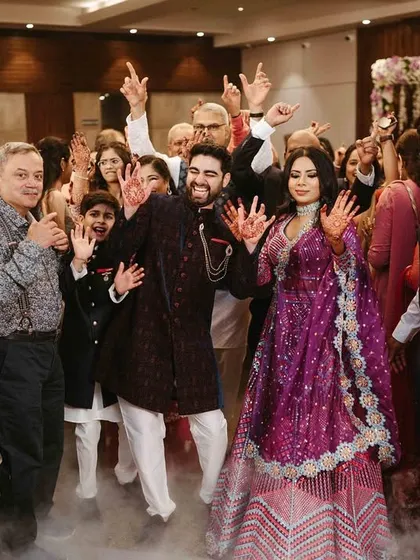 The couple making a grand, high-energy entrance to their sangeet, surrounded by family and a cloud of smoke.