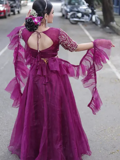 The back view of this stunning wine-colored organza lehenga, featuring a keyhole back and dramatic ruffled sleeves for a modern, high-fashion statement.