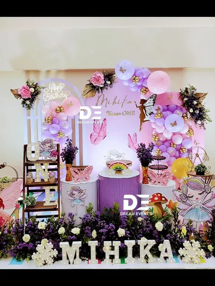 A full view of Mihika's enchanting fairy-themed birthday stage. The design includes multiple pedestals for cakes and props, fairy cutouts, and personalized name blocks.