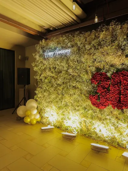 A beautiful floral wall serves as the backdrop for a 30th-anniversary party. The wall is made of delicate white and green foliage, with the number "30" created from vibrant red roses.