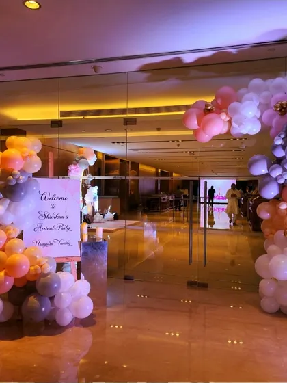 A whimsical balloon arch in pastel shades of orange, grey, and white welcomes guests to a baby's arrival party. The design is modern, soft, and celebratory.