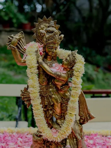 A brass statue of Radha and Krishna, adorned with a floral garland.