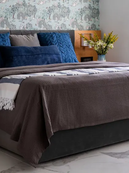 The bed in the Jaipur master bedroom, dressed in a textured grey bedspread and deep blue pillows. The white marble flooring adds to the cool, refreshing feel of this elegant and tranquil space.