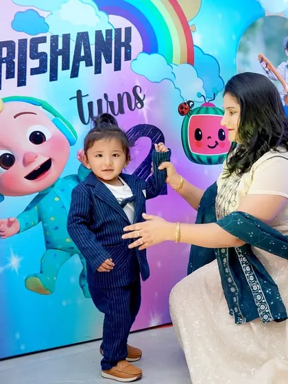 A mother helps her son, dressed in a smart suit, pose in front of a colorful Cocomelon birthday banner. We always make time for those cherished parent and child photos.