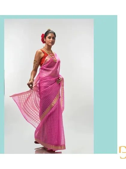 The mystic pink organza saree is captured in motion, showing its beautiful flow and the playful pattern of gold zari checks.