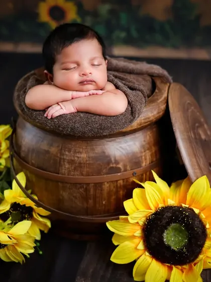 A rustic setup featuring a baby sleeping in a wooden barrel, surrounded by bright sunflowers.