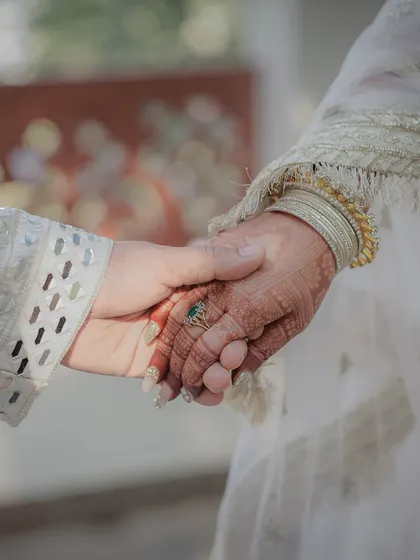 A close-up shot of the couple holding hands, focusing on the intricate details of their outfits and the bride's henna.