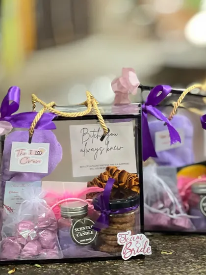Two bridesmaid hampers shown side-by-side, featuring a purple and pink color scheme. The "Team Bride" sticker adds a fun, unifying touch.