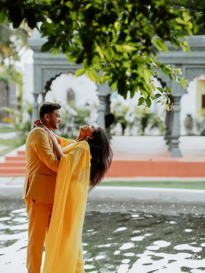 A romantic moment by the water, the bride leaning back in the groom's arms, her yellow saree a splash of sunshine.